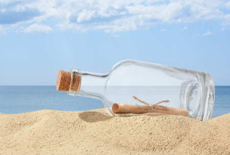 Corked bottle with rolled letter inside on sand near seaの写真素材
