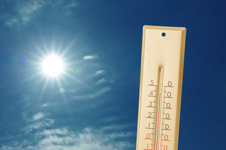 High temperature on thermometer against blue sky with clouds and bright sun. Extremely hot weather