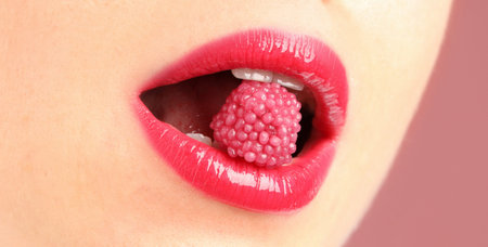 Woman with beautiful lips makeup and raspberry candy on dusty pink background, closeup