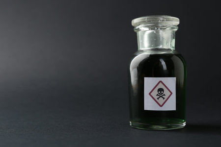 Bottle of poison with warning sign on gray background, closeup. Space for text