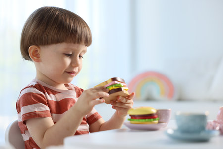 Cute little boy playing with toy tea set at table indoors. Space for textの写真素材