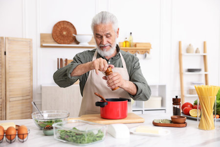 Elderly man cooking at white marble table in kitchenの写真素材