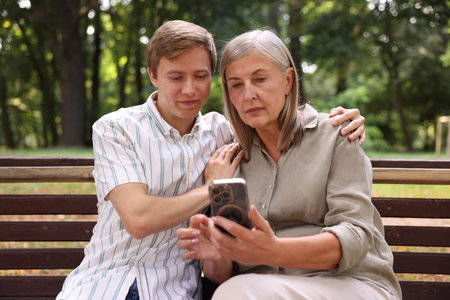 Mother and her son using smartphone on bench in park