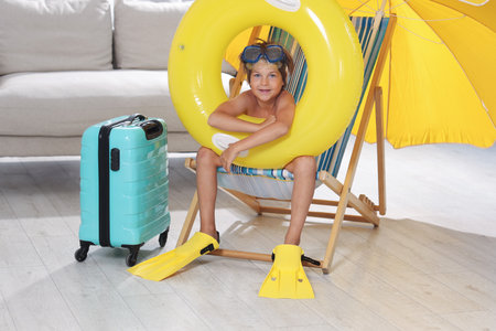 Dreaming about vacation at sea. Little boy with diving mask, flippers and inflatable ring on deckchair indoorsの写真素材
