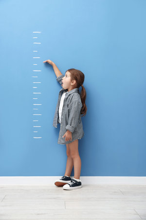 Cute little girl measuring her height near blue wall
