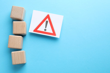 Blank cubes and sheet of paper with warning sign on light blue background, flat lay. Space for textの写真素材