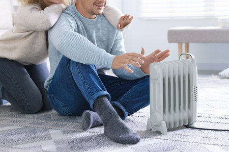 Happy couple near electric heater on floor at home, closeup