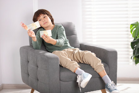 Boy with pocket money in armchair at homeの写真素材