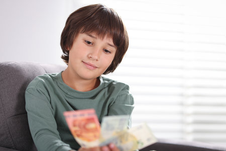Boy with pocket money in armchair at home. Space for textの写真素材