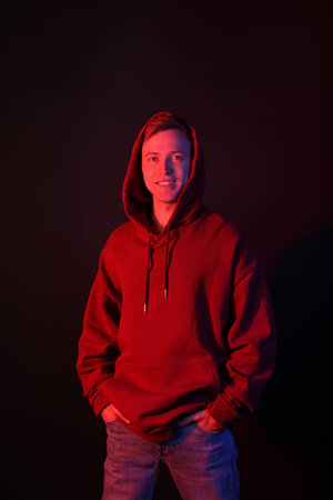 Portrait of smiling man wearing hoodie in neon lights against black background