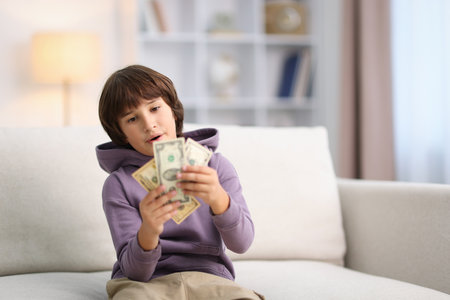 Boy with pocket money on sofa at home. Space for textの写真素材