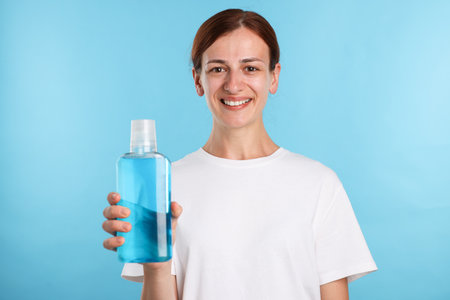 Woman rinsing mouth with mouthwash on light blue backgroundの写真素材