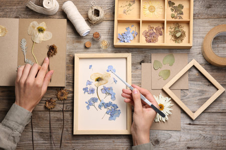 Woman putting dry flowers into picture frame at wooden table, top viewの写真素材