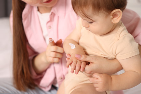 Mother applying cream onto her baby's arm on bed at home, closeupの写真素材