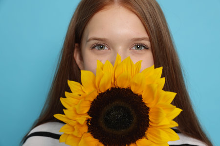 Teenage girl with sunflower on light blue backgroundの写真素材