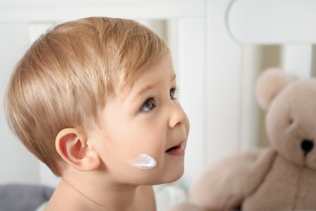 Cute baby with cream on his face in crib at homeの写真素材