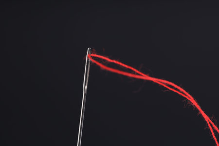 Sewing needle with red thread on black background, closeup