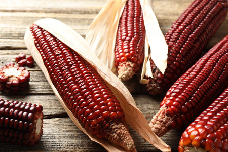 Ripe red corn cobs on wooden table, closeup