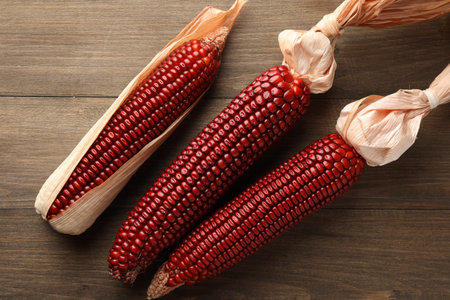 Ripe red corn cobs on wooden table, flat lay