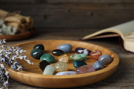 Different beautiful gemstones and book on wooden table, closeup