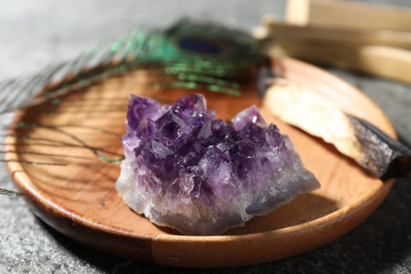 Beautiful amethyst gemstone and peacock feather on gray table, closeup