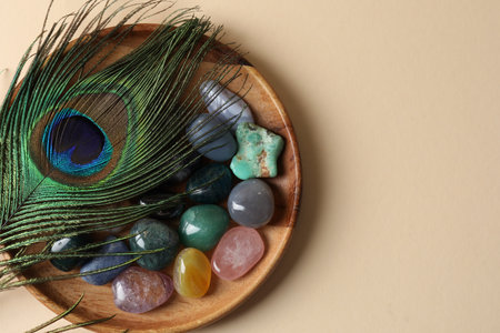 Different beautiful gemstones and peacock feather on beige background, top view. Space for textの写真素材