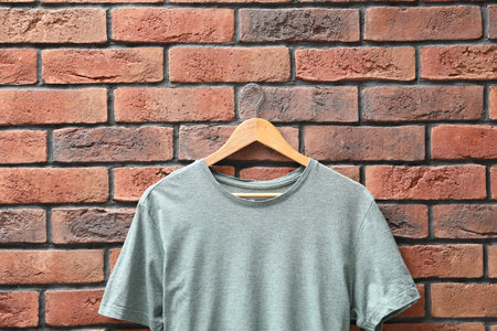 Hanger with gray t-shirt against red brick wall, closeup. Mockup for design