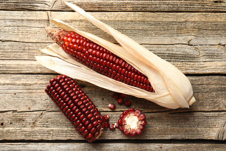 Ripe red corn cobs on wooden table, flat lay