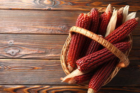 Ripe red corn cobs in basket on wooden table, top view. Space for text
