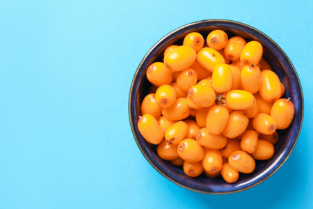 Ripe sea buckthorn berries in bowl on light blue background, top view. Space for text