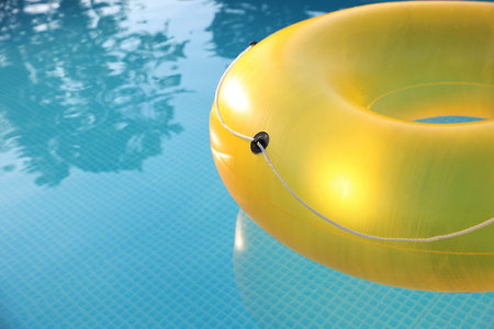 Yellow inflatable ring in swimming pool outdoors, closeup. Space for text