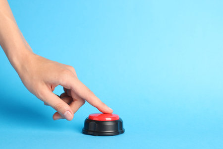 Woman pressing red button on light blue background, closeup. Space for text