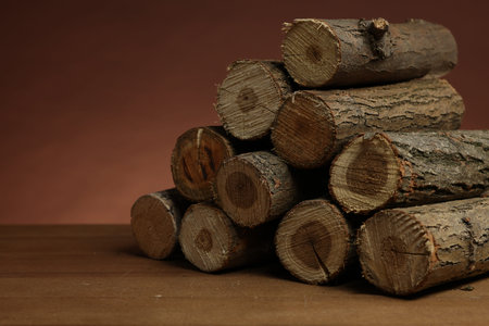 Pile of cut firewood on wooden table against brown background, closeup. Space for text