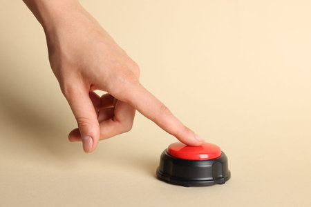 Woman pressing red button on beige background, closeup