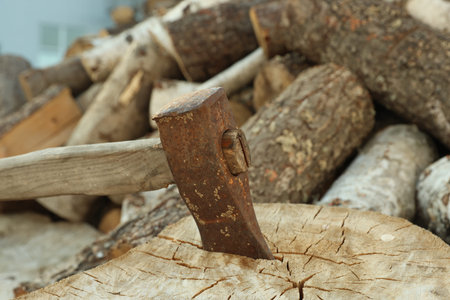 Ax in stump and pile of cut firewood outdoors, closeup