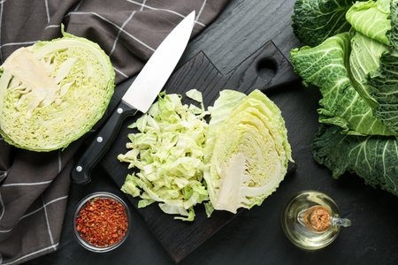 Cut fresh Savoy cabbage, spices, oil and knife on black table, flat lay