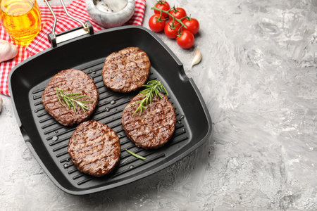 Pan with grilled patties, tomatoes and spices on gray table. Space for text
