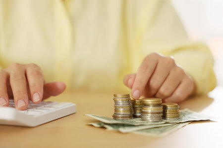 Woman counting money on calculator at wooden desk, closeup