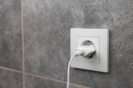 USB adapter with cable plugged into electric socket on gray wall, closeup. Space for text