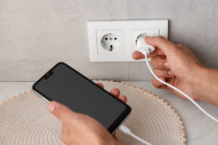 Man plugging smartphone into power socket indoors, closeup