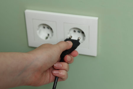 Woman inserting electric plug into power socket on green wall, closeup