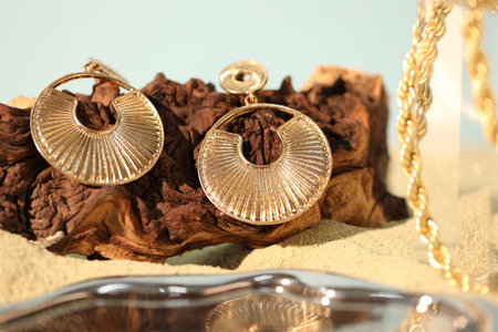Beautiful gold jewelry and wood on sand, closeup