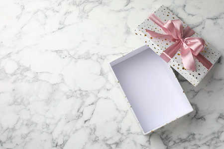 Opened gift box with beautiful lid on white marble table, top view. Space for text