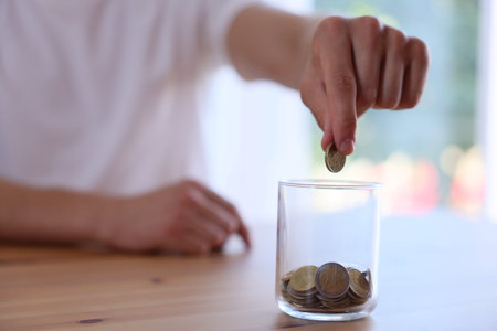 Man putting money into jar at wooden table indoors, closeup