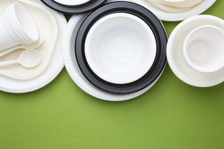 Set of disposable plastic tableware on light green background, flat lay. Space for text