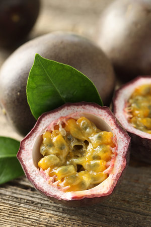 Fresh passion fruits and green leaves on wooden table, closeup