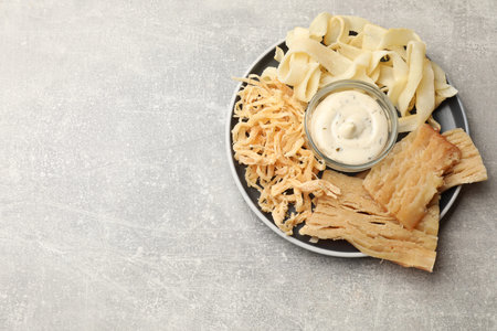 Tasty dried squid and sauce on gray table, top view.