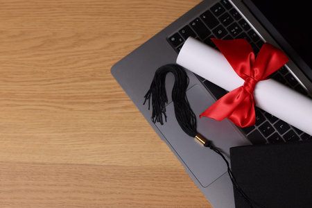 Graduation cap, laptop and diploma on wooden table, flat lay. Space for textの写真素材