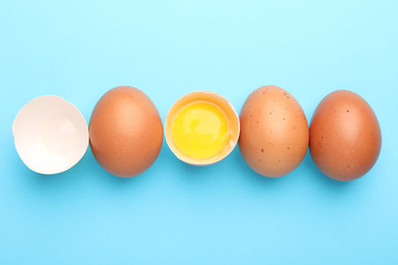 Whole and broken chicken eggs on light blue background, flat lay