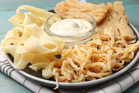 Tasty dried squid and sauce on light blue wooden table, closeup